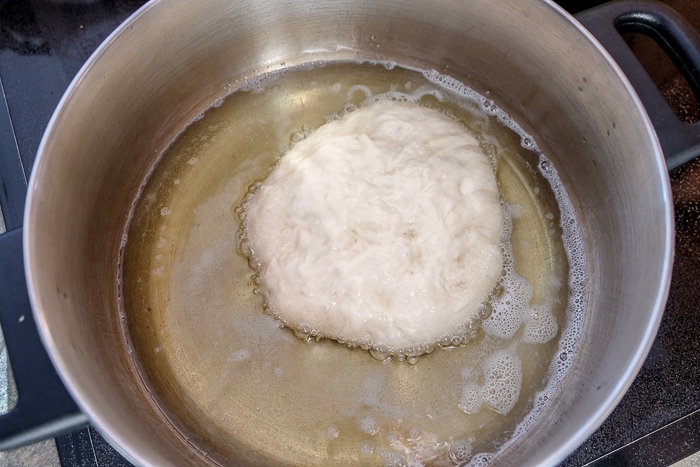 bubbling frying langos dough in oil in metal pot on stove top
