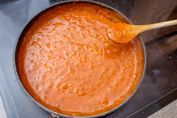 thick red bravas sauce in frying pan on stove top with wooden spoon