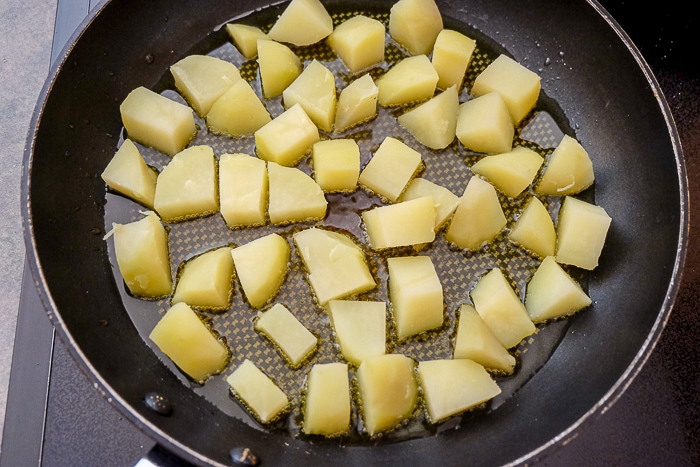 diced potato pieces frying in oil in frying pan on stove