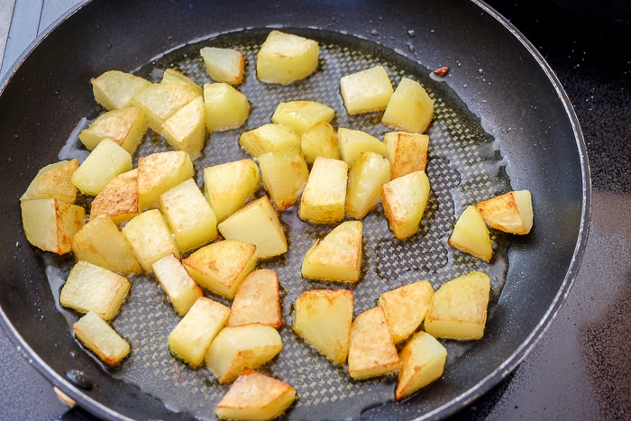 browning pieces of potatoes frying in frying pan on stove