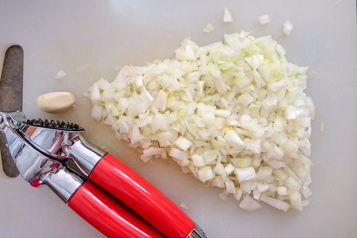 chopped onions on cutting board beside garlic press