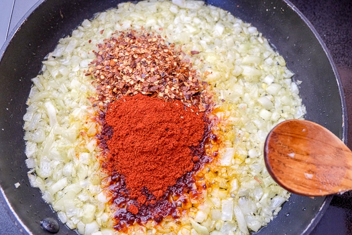 red spice on fried onion in frying pan with wooden spoon