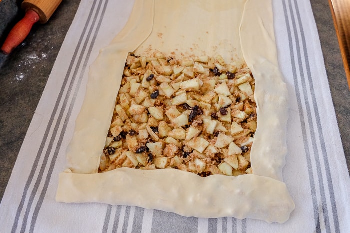 apple strudel on dish towel with filling ready to be rolled
