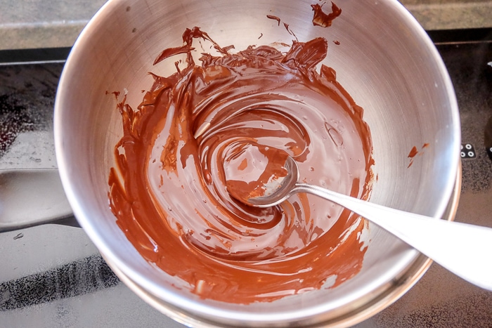 melted dark chocolate in bowl with spoon on stove top