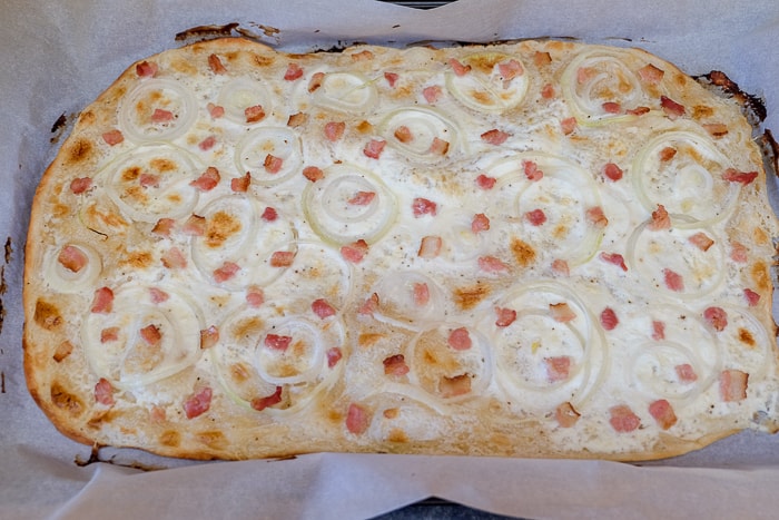 cooked flammkuchen on parchment paper on oven pan