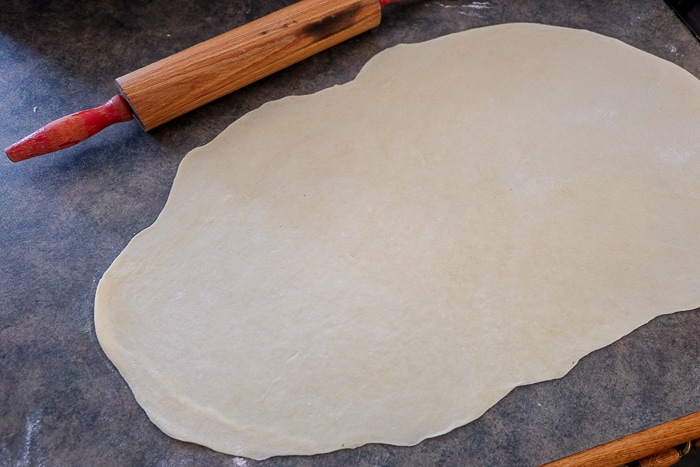 rolled out flammkuchen dough on counter with rolling pin beside