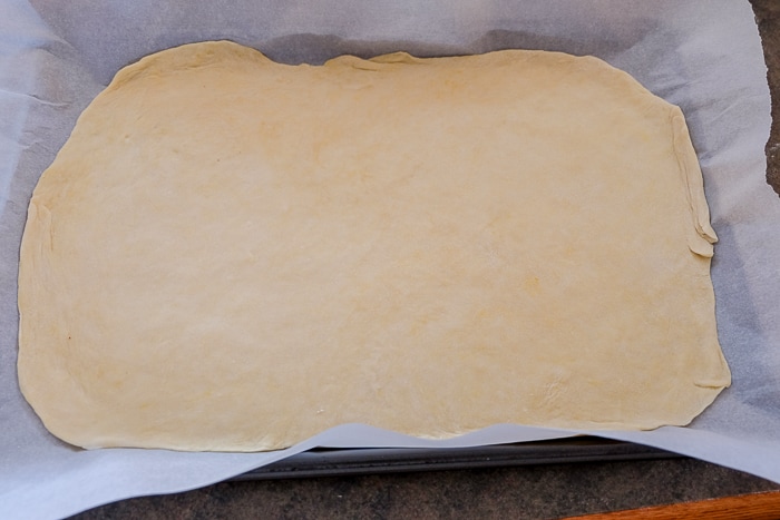 flammkuchen crust spread out on parchment paper oven tray