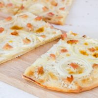 white creamy flammkuchen pieces with bacon on top on wooden board