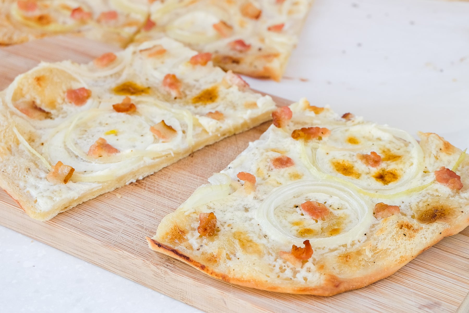 white creamy flammkuchen pieces with bacon on top on wooden board