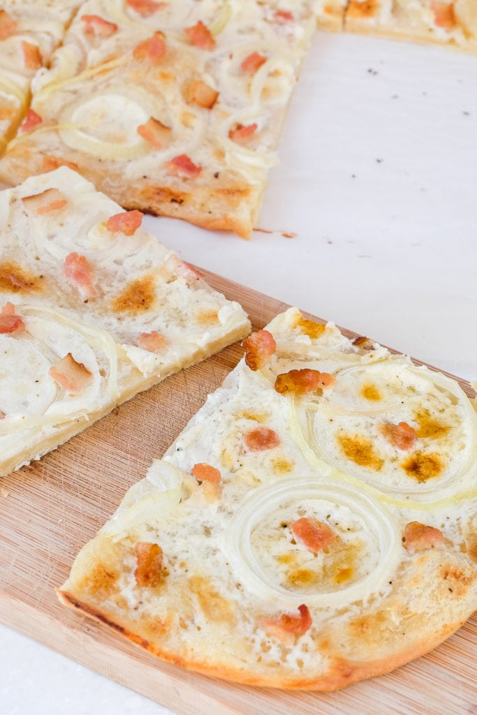 pieces of flammkuchen cut on wooden board on white counter