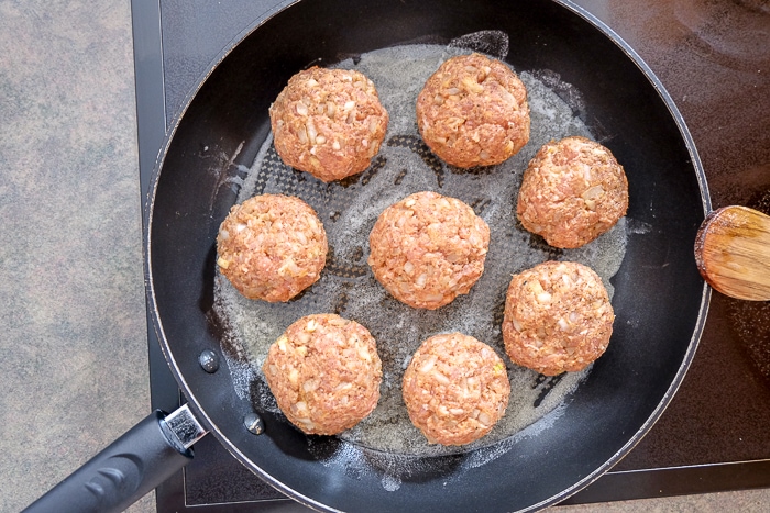 raw meatballs frying in butter in frying pan on stove