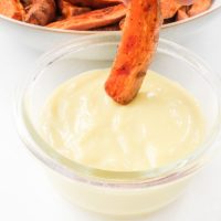 sweet potato fry dipped into homemade aioli in small glass dish