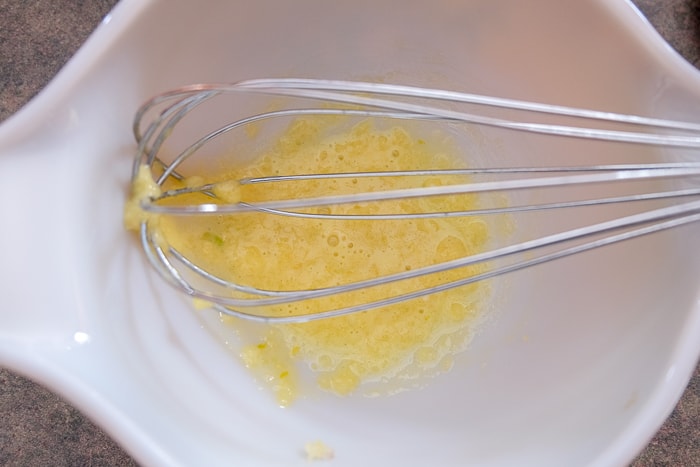 silver whisk mixing egg yolk and vinegar in bowl