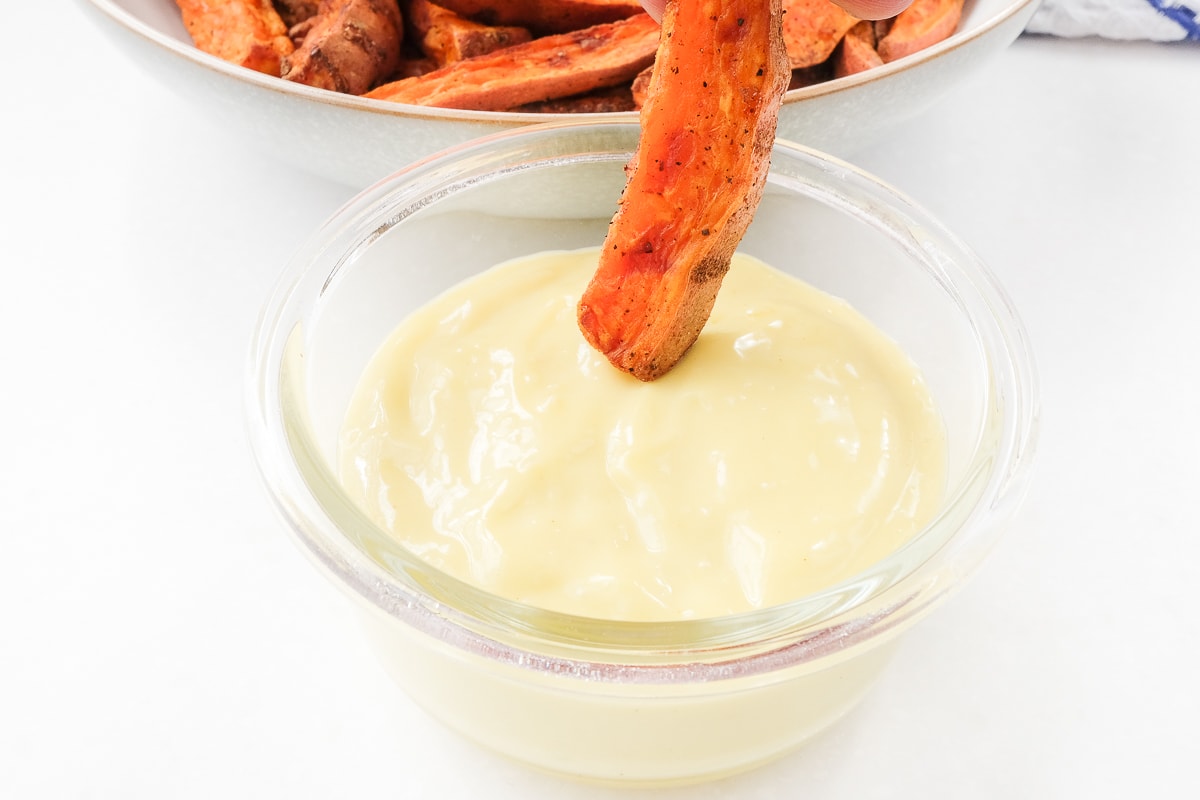 sweet potato fry dipped into homemade aioli in small glass dish