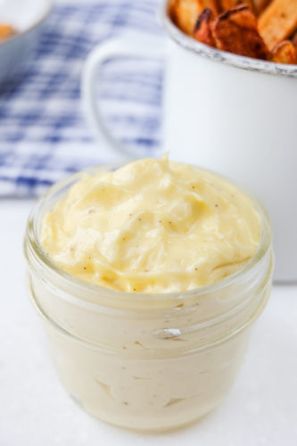 homemade mayonnaise in glass jar with cup of fries behind