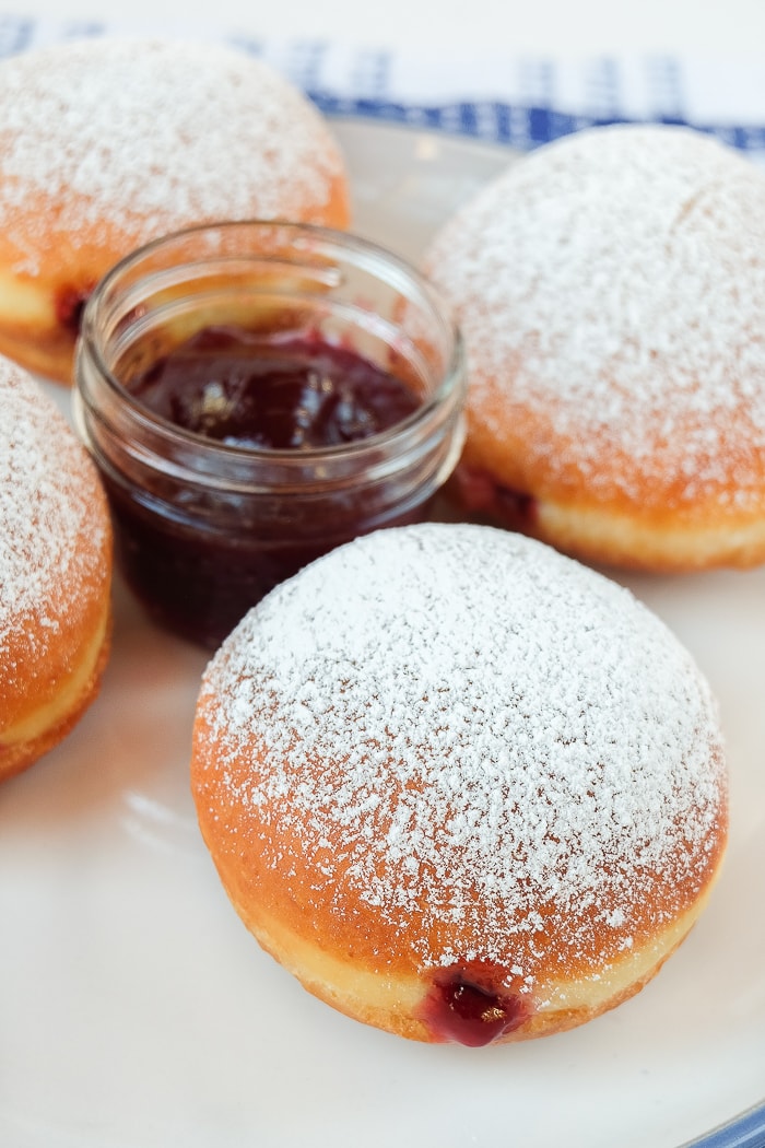 four round krapfen donuts with jar of jam on plate