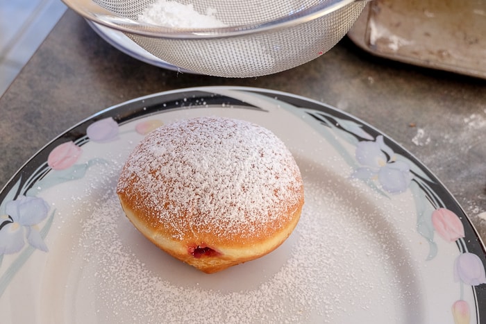 sprinkling powdered sugar on krapfen donut on plate