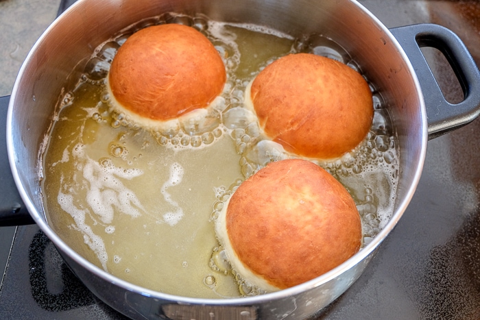 three krapfen donuts floating in pot of frying oil