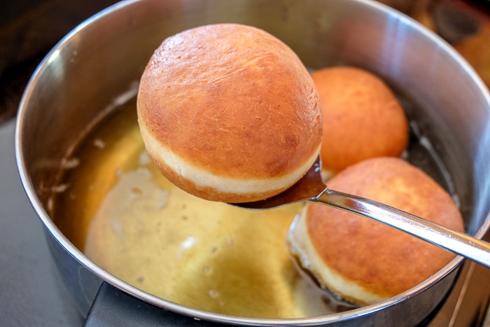 krapfen donut on straining spoon being lifted from silver pot of oil