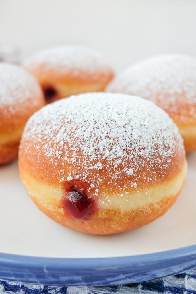 jelly filled donuts with powdered sugar on blue and white plate