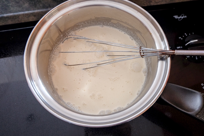 boiling milk and cream in silver pot on stove with whisk