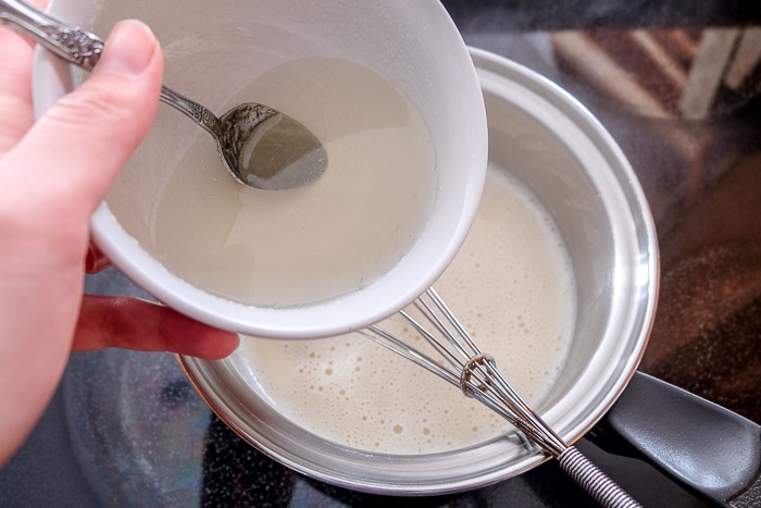 pouring gelatin into silver pot on stove with whisk