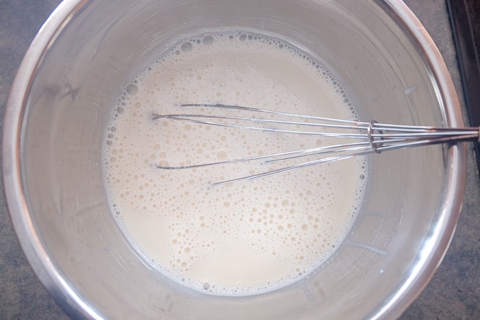 mixing bowl full of cooling panna cotta with whisk inside