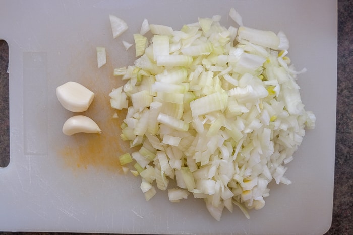 chopped onions and whole garlic on white plastic cutting board