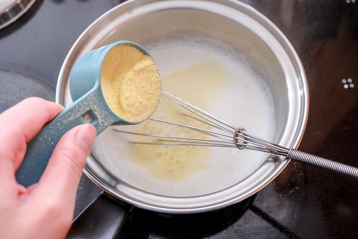 pouring semolina into pot of boiling milk with whisk