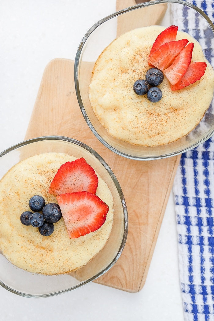two glass bowls of semolina pudding with berries on wooden board