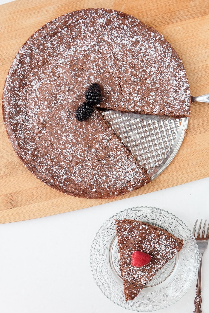 swedish chocolate cake with berries on wooden board with slice cut on plate beside fork