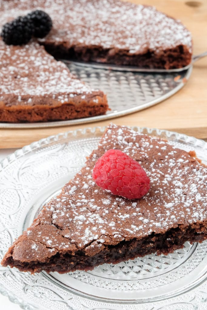 slice of thin swedish chocolate cake on plate with raspberry on top and large cake behind