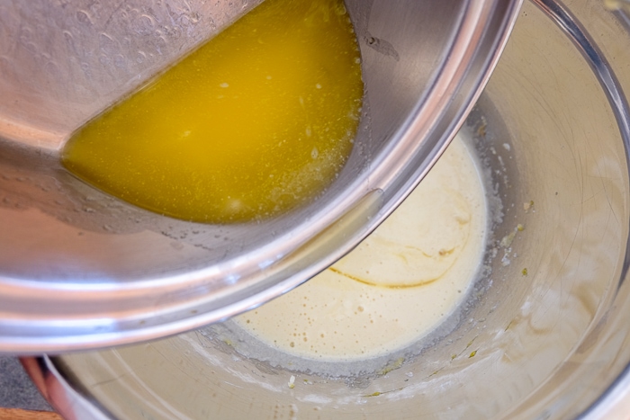 pouring melted butter into bowl of wet batter on counter