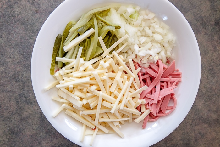 ingredients for wurstsalat in white bowl without dressing on counter