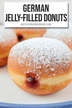 deep-fried balls of dough with red jam in the middle and powdered sugar on top on plate with blue rim and text overlay saying "German jelly-filled donuts"