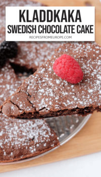 Slice of chocolate cake with icing sugar and raspberry on top and rest of cake in background plus text overlay saying "Kladdkaka Swedish chocolate cake"