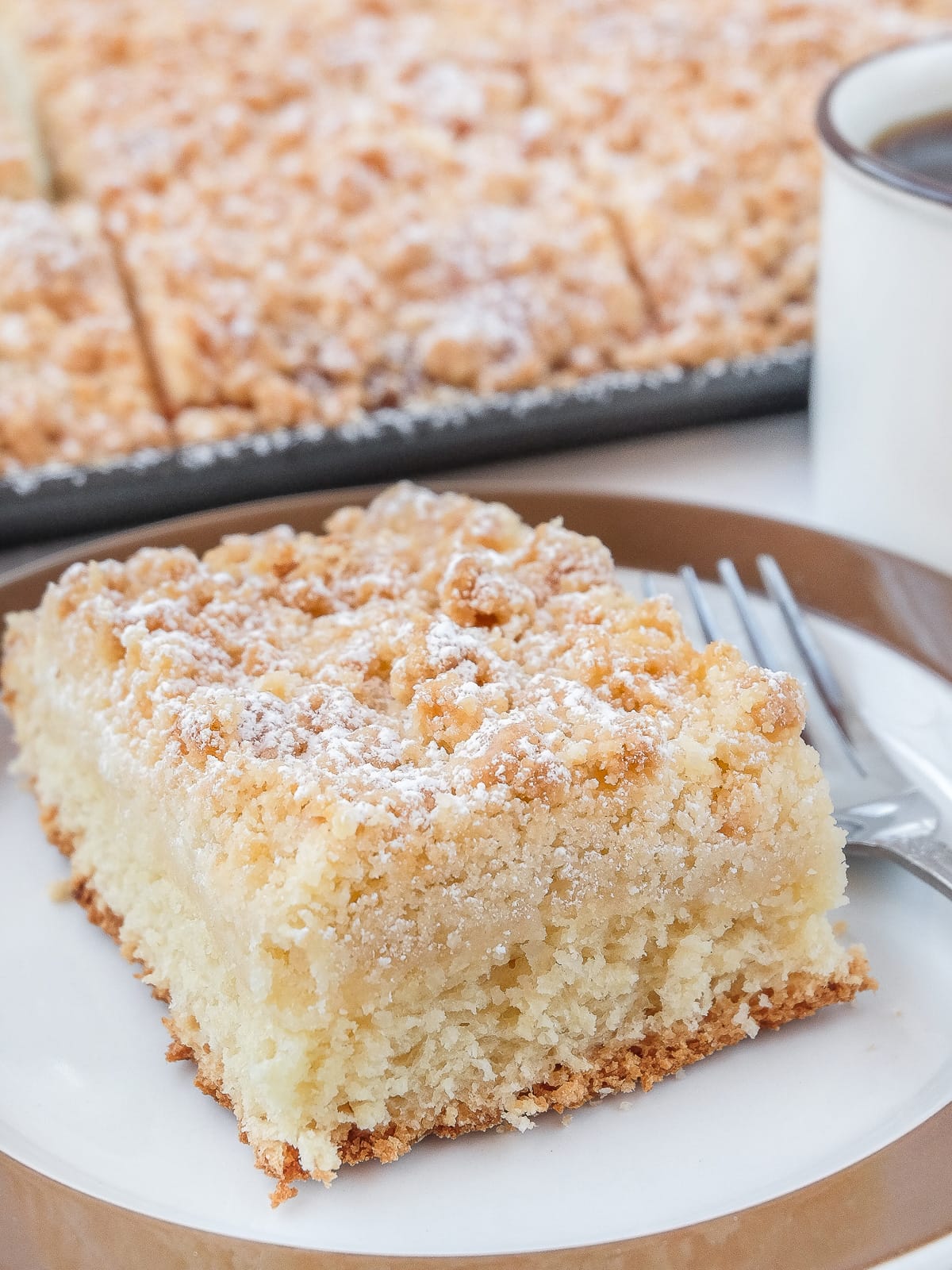 piece of coffee cake with streusel on plate with brown rim and cake in background