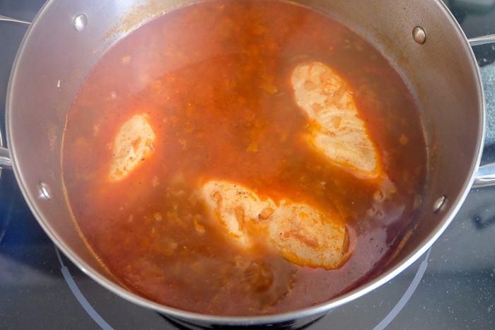 chicken breasts cooking in red paprika broth