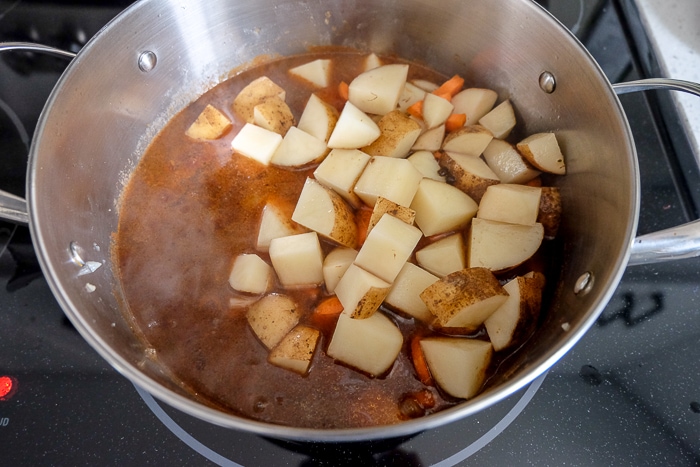 raw potatoes added to large silver pot of goulash