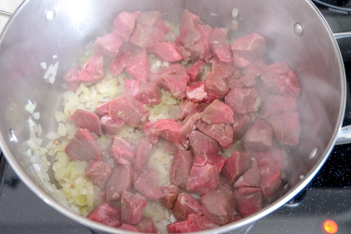 beef and onions cooking in large silver pot