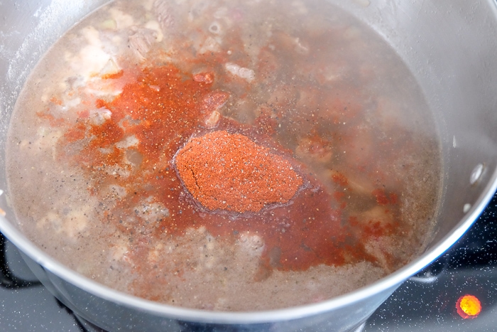 paprika spice on top of goulash broth in silver pot on stove