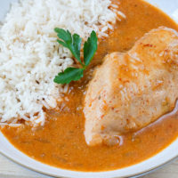 bowl of paprika chicken with rice and red broth with parsley