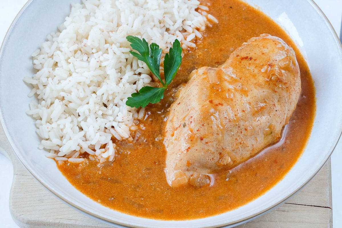 bowl of paprika chicken with rice and red broth with parsley