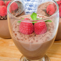 chocolate panna cotta in glasses with raspberries and mint leaves on top on wooden board