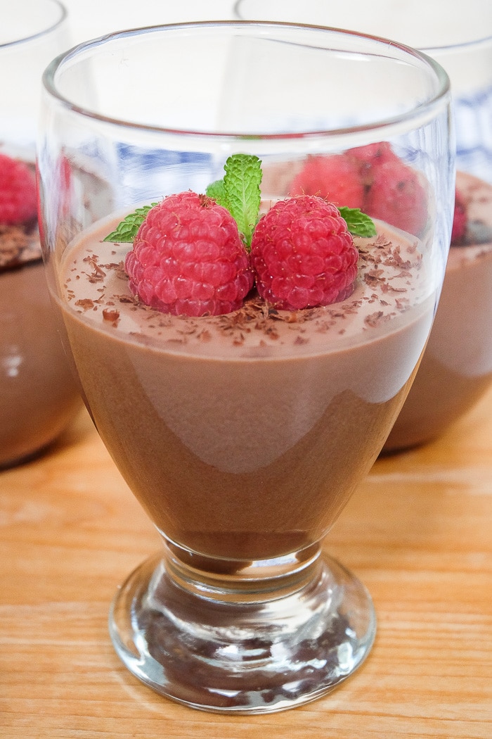 glass of chocolate panna cotta with raspberries on top sitting on wooden board