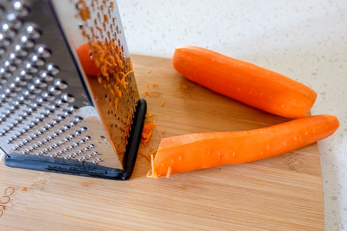 raw carrot on wooden board with metal grater beside