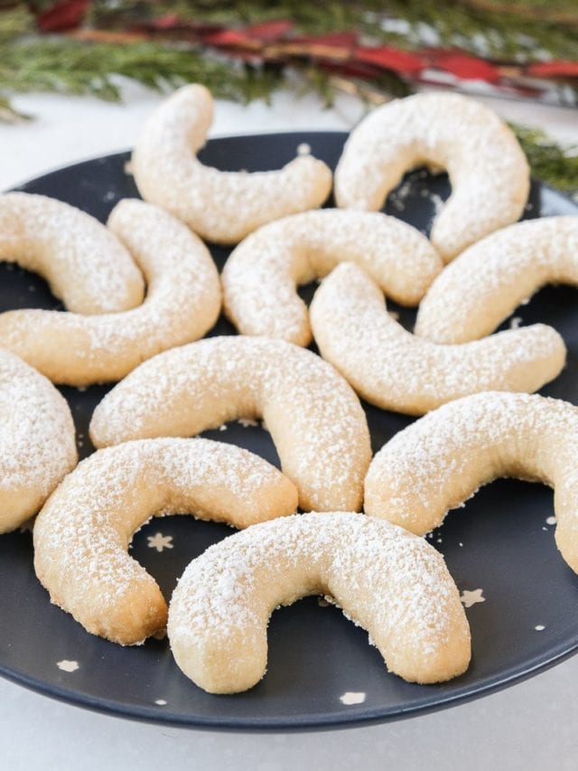vanilla crescent cookies with icing sugar on dark blue plate.