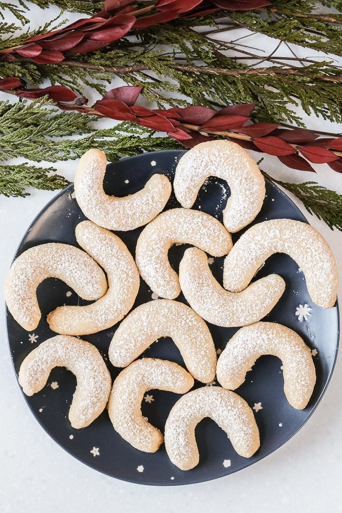 vanilla crescent cookies on blue plate with red and green bracnhs above