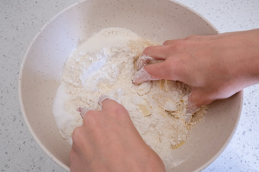 two hands mixing cookie dough in white bowl on counter top