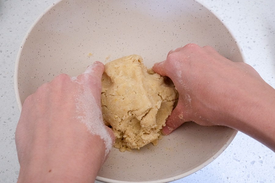 hands mixing ball of cookie dough in bowl on white counter